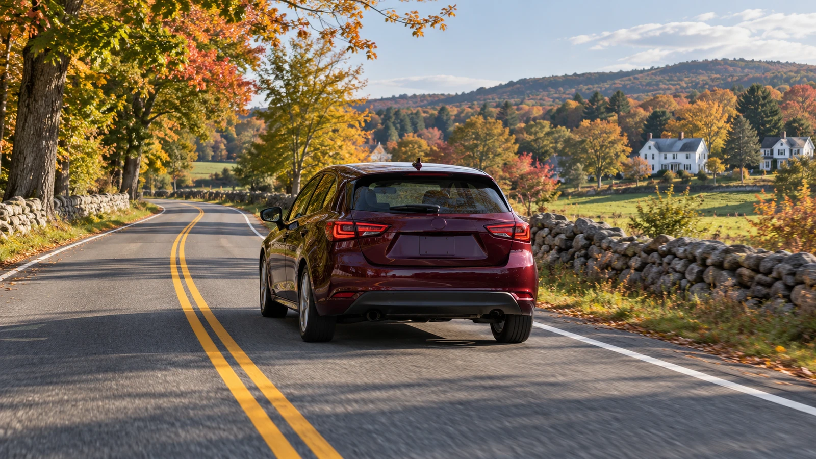 Burgundy hatchback on a two-lane road bordered by stone walls and autumn trees.